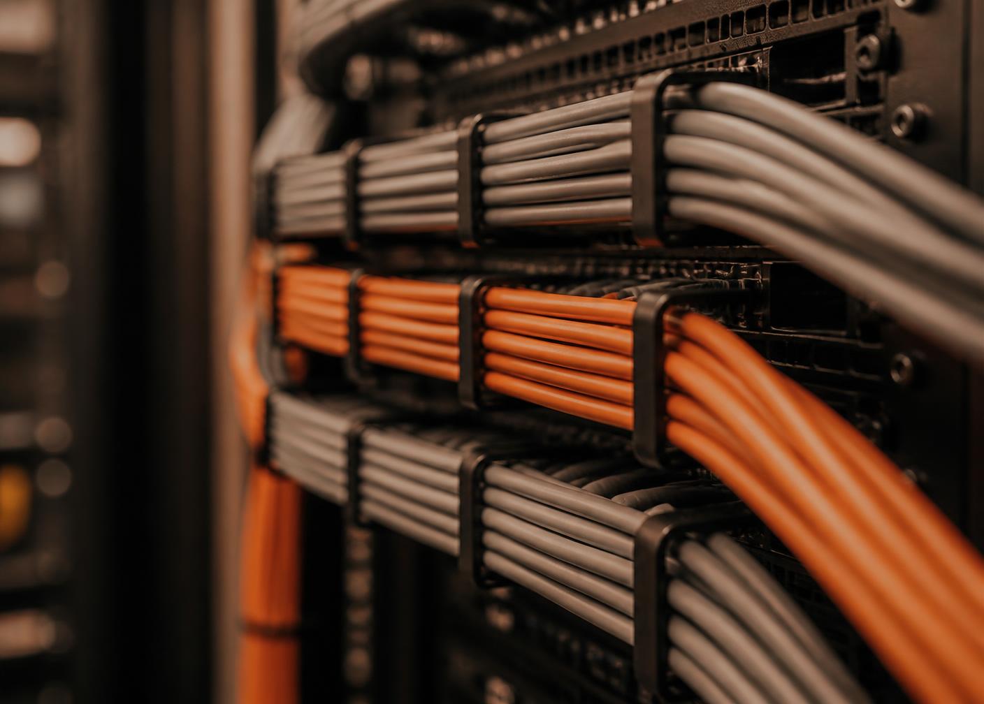 Structured bundles of grey and orange network cables routed through a rack panel